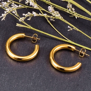 Macro view of gold chunky C-shaped hoop earrings with polished finish on stone surface