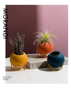 Three spherical Morandi ceramic vases with gold metal stands in high-contrast light