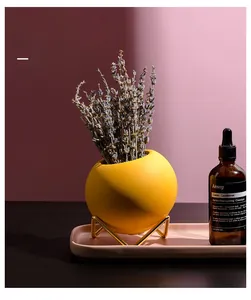 Detail of a matte yellow circular ceramic vase on a golden geometric metal stand base