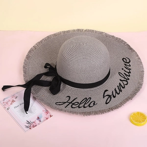 Detail of grey straw sun hat featuring black bow and Hello Sunshine embroidery