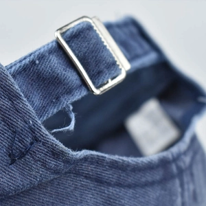 Detail showing the adjustable silver metal buckle on washed navy denim baseball cap