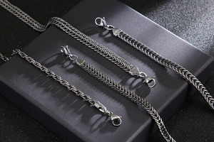 Macro detail of braided stainless steel chain with lobster clasp on a black pedestal