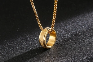 Macro detail of golden spinning ring pendant with engraved Sanskrit mantra and box chain
