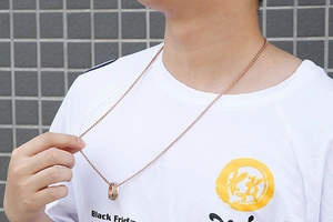 Close-up of rose gold spinning ring pendant on box chain worn by a male model