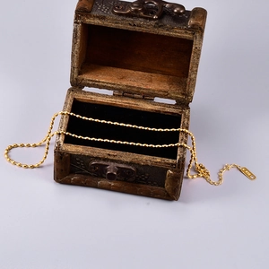 Detail of 18K gold bead chain necklace showing K18 hallmark on metal tag near a wooden box