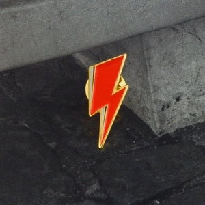 Detailed macro view of the red and blue lightning bolt enamel pin on grey stone texture