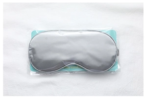 Close-up of grey satin sleep mask in individual packaging on white fabric