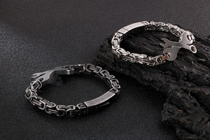 Détail de bracelets en acier titane avec boucle clé sur fond texturé noir et charbon