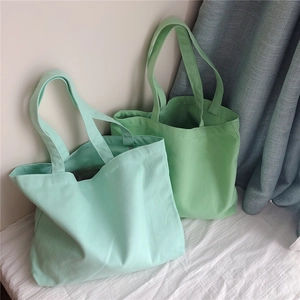 Détail de sacs cabas en toile vert menthe et sauge sur fond de literie blanche douce