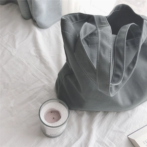 Détail des coutures d'un sac cabas en toile gris foncé sur fond de tissu blanc