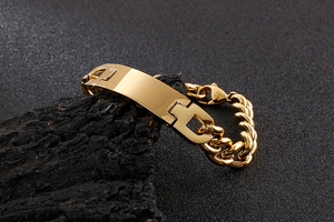 Close-up of a polished gold ID tag bracelet with a thick cuban chain on a stone pedestal