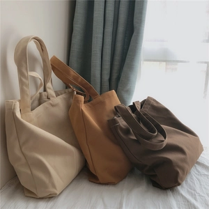 Trois sacs cabas en toile de couleurs crème, fauve et marron foncé sous une lumière naturelle