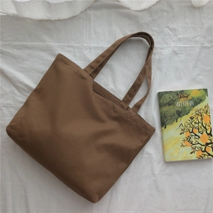 Vue à plat d'un grand sac cabas en toile de coton marron sur un tissu blanc texturé