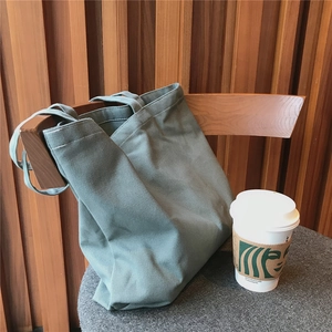 Sac fourre-tout en toile vert sauge suspendu à une chaise en bois vintage avec café