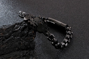 Detail of a black skull biker bracelet for men on rock, featuring punk steel chain texture