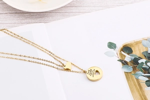 Detail view of gold double-layer necklace with heart pendant and engraved round plate