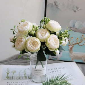 Close-up of artificial cream peonies and roses in a vase with newspaper background