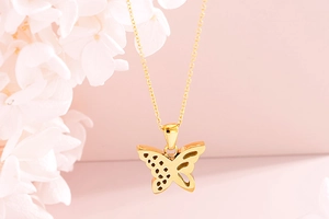Close-up of golden butterfly hollow pendant necklace set against floral background