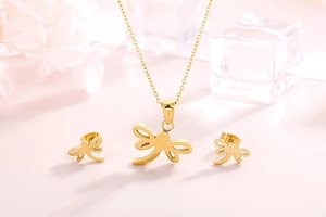 Golden dragonfly necklace and stud earrings set on pink background with white flowers