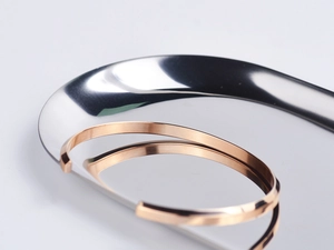 Polished rose gold C-shape open bangle resting on a reflective silver tray detail