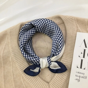 Detail of blue houndstooth silk scarf tied on a beige sweater neckline with premium sheen