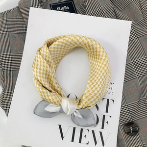 Detailed close-up of yellow and white houndstooth silk scarf tied in a bow on a blazer