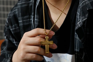 Close-up of a gold hip hop cross pendant necklace with fine texture on a male model