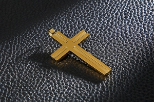 Macro view of a gold-plated double-layer cross pendant on textured black leather