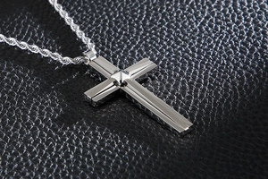 Macro shot of silver cross pendant and rope chain on a black textured leather background