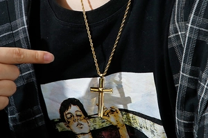 Close-up of double layer gold cross pendant necklace with twisted rope chain worn by a model