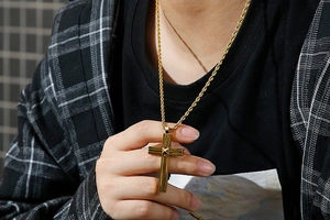 Close-up of golden stainless steel cross pendant necklace on a twisted rope chain