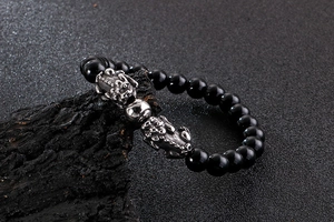 Macro detail of black beaded bracelet with silver Pixiu charm on dark wood stand