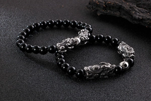 Detailed view of black beaded bracelets with silver Pi Xiu charms on dark texture