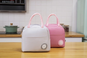 Detail of insulated canvas lunch bag with zipper and round cartoon patch on wood table