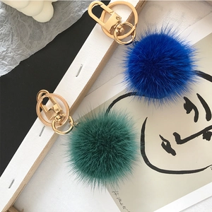 Close-up of blue and dark green mink fur balls with gold alloy keychains on white wood