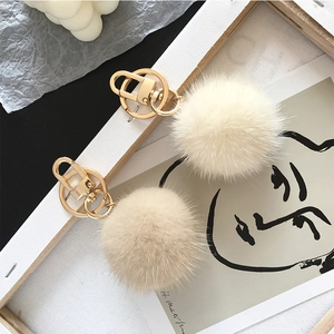 Detailed close-up of fluffy cream mink fur pompoms with gold metal keychain clips