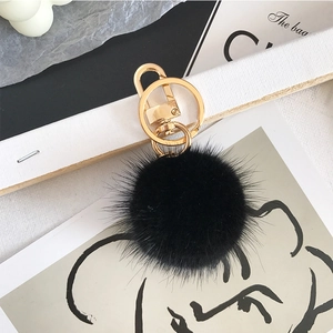 Close-up of black mink fur pompom keychain with golden metal spring buckle on art magazine