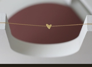 Detail view of a minimalist gold heart pendant on a delicate chain jewelry piece