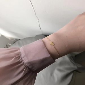 Detailed view of a gold heart charm bracelet on wrist with pink pleated sleeve fabric