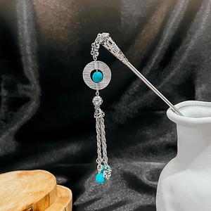 Close-up of silver hair stick with turquoise beads and tassel in vintage ethnic style