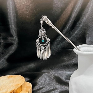 Detail of silver ethnic hair pin featuring turquoise beads and tapered metal tassels
