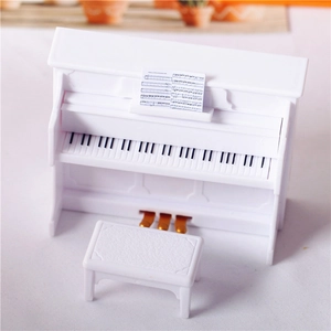 Miniature white upright dollhouse piano with matching stool and sheet music on white background