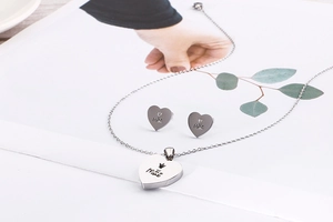 Macro shot of silver hollow heart necklace and earrings with engraved Mae text