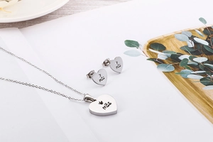 Detailed view of silver heart jewelry set with Mãe engraving on necklace and earrings