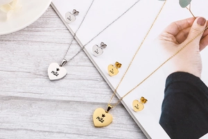 Close-up of gold and silver heart necklaces with Mae engraving and crown detail