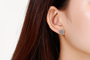 Close-up of silver heart-shaped stud earring with M&S crown engraving on ear