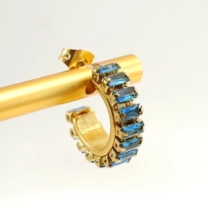 Macro shot of 18K gold C-shaped earrings set with rectangular blue crystals on a stand