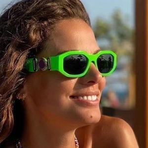 Close-up of bright green rimless sunglasses with iconic gold medallion on the temple