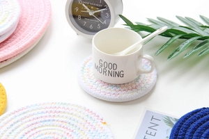 Close-up of white woven cotton coasters with colorful stitching on a breakfast table