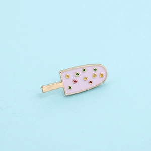 Close-up of a pink ice cream enamel brooch with golden trim and colorful dots details